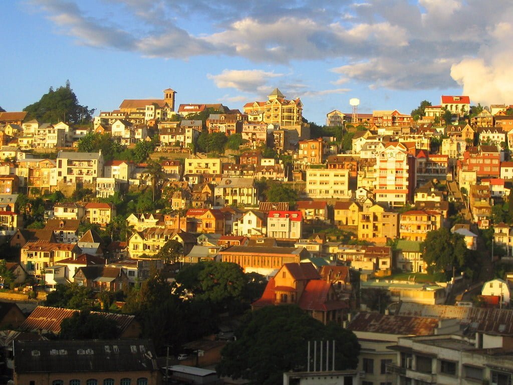 Hillside view of a densely populated town with multi-story buildings at sunset, casting warm hues over the architecture.