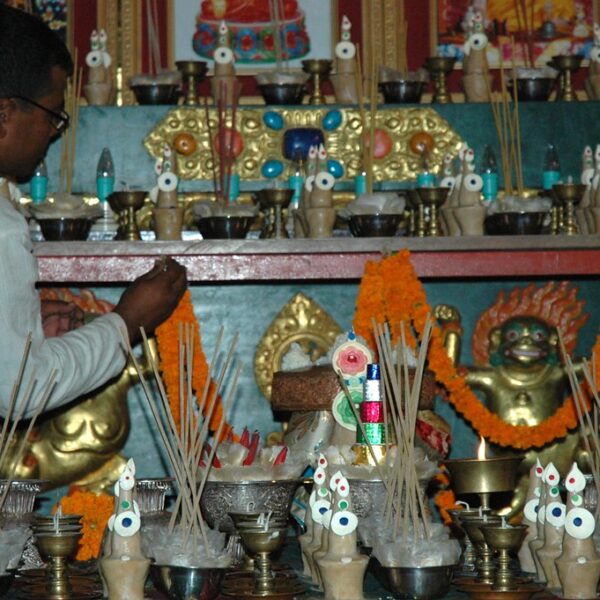 A person lighting incense sticks at an altar adorned with marigold flowers, Buddhist statuettes, and various ritual items.