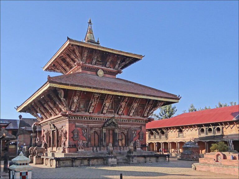 Alt text: An intricate traditional Nepalese pagoda-style temple with detailed wood carvings and tiered roofs against a clear blue sky.