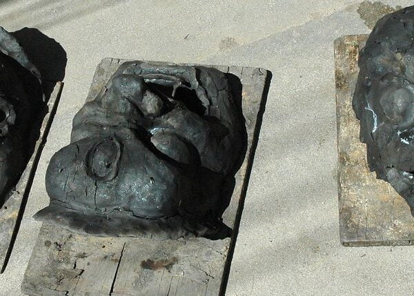 Three damaged, grotesque masks lying on wooden boards on a concrete surface.