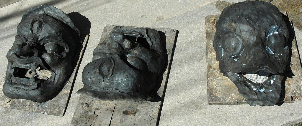 Three damaged, grotesque masks lying on wooden boards on a concrete surface.