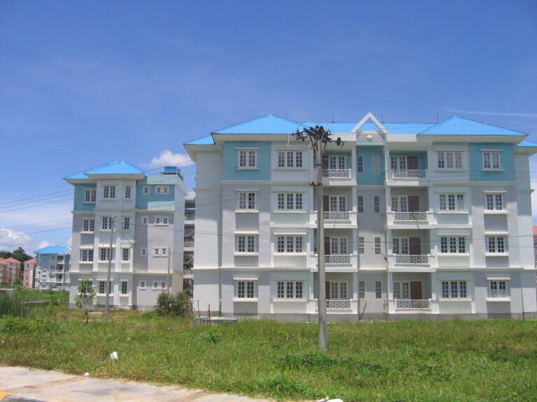 A row of light blue multi-story residential buildings under a clear blue sky with a utility pole in the foreground.