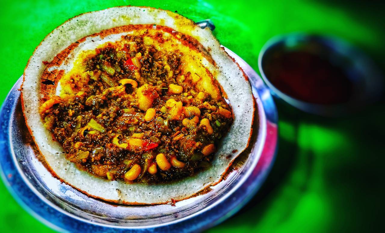 A plate of Ethiopian injera topped with a spicy stew containing lentils and vegetables, with a side of sauce on a green background.