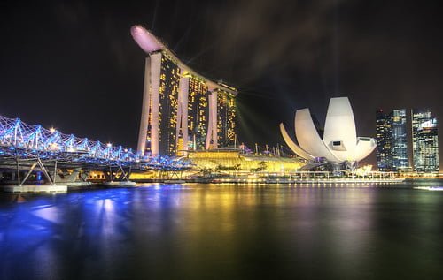 Night view of Marina Bay Sands and the ArtScience Museum in Singapore with illuminated skyscrapers and reflections on the water.