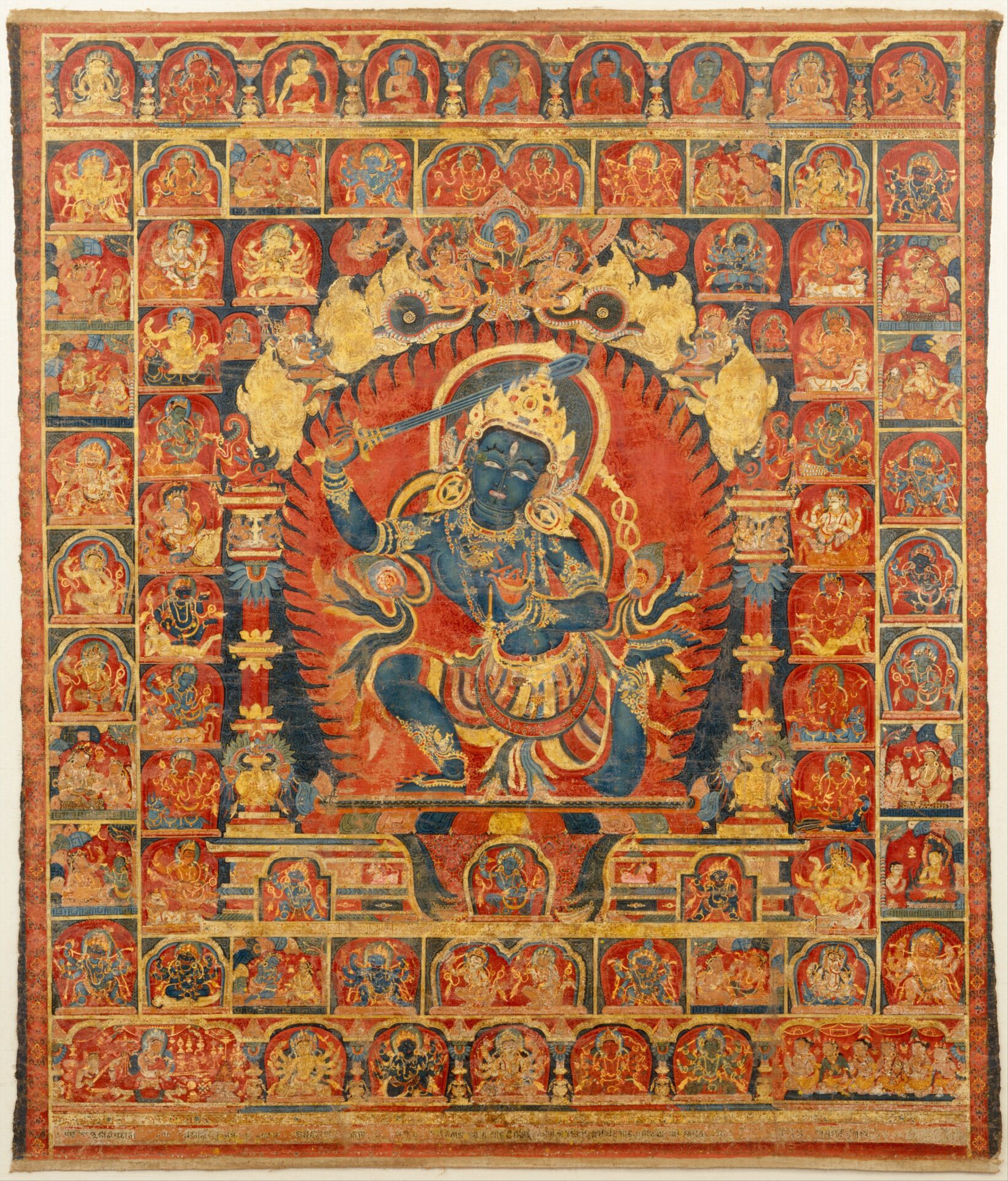 An intricate traditional Tibetan thangka painting depicting a multi-armed, blue deity surrounded by a fiery halo, with numerous smaller figures in detailed compartments around the central figure.