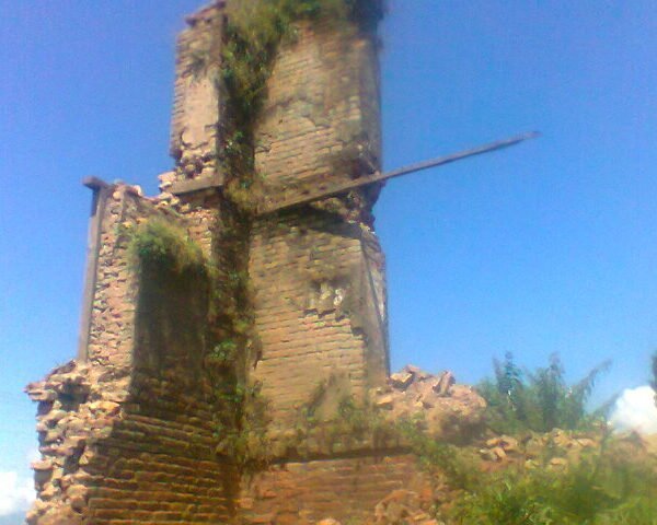 Ruins of an old brick tower overgrown with vegetation under a blue sky.