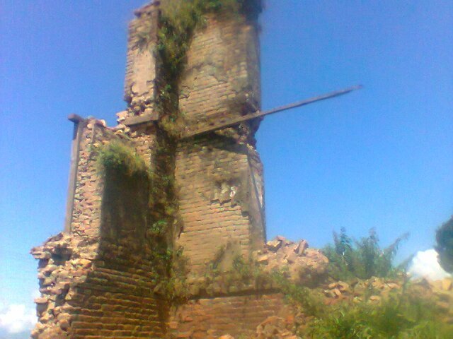Ruins of an old brick tower overgrown with vegetation under a blue sky.