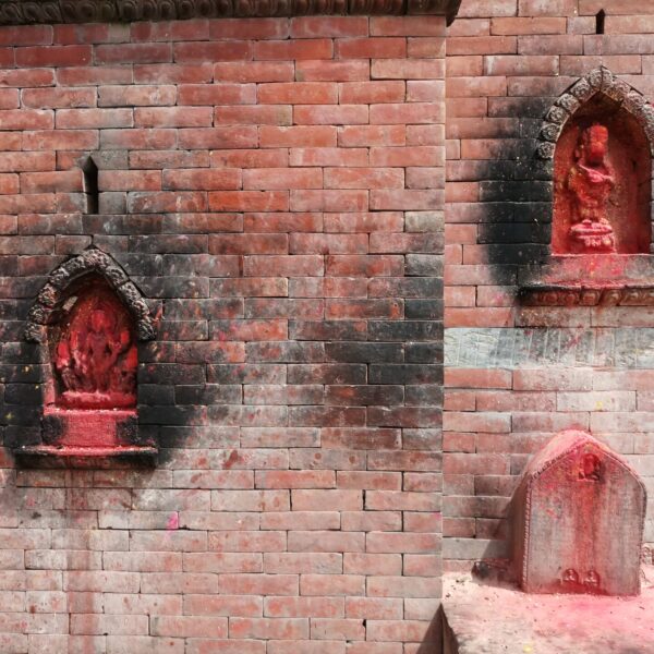 Three religious shrine statues with red pigment set into alcoves of a brick wall, exhibiting signs of worship.