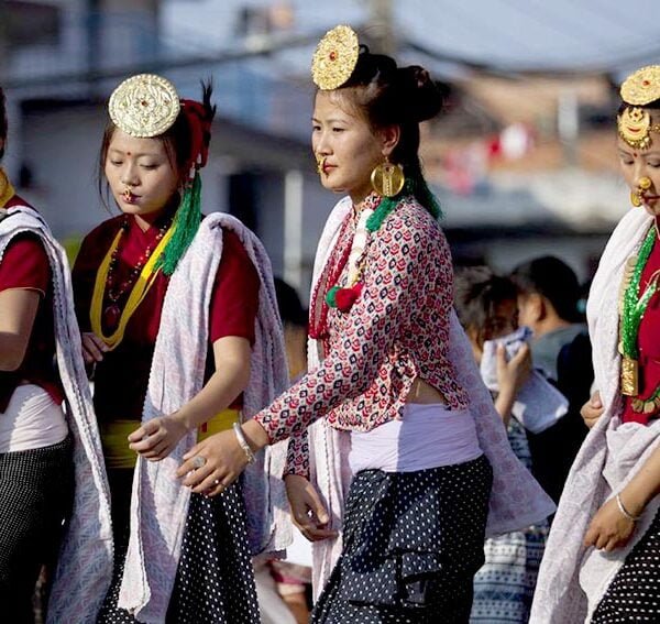A group of four women dressed in traditional attire with gold headpieces, large earrings, and beaded necklaces performing a dance or participating in a cultural procession.
