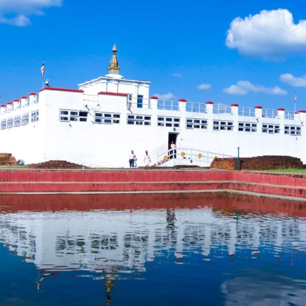 White traditional building with a gold spire reflecting in water, under a blue sky with white clouds, and visitors nearby.