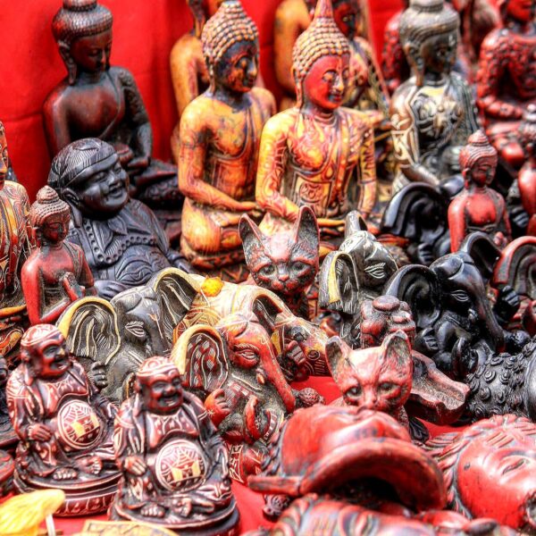 A collection of intricately carved wooden figurines, including several depictions of the Buddha and various animals, displayed against a red background.