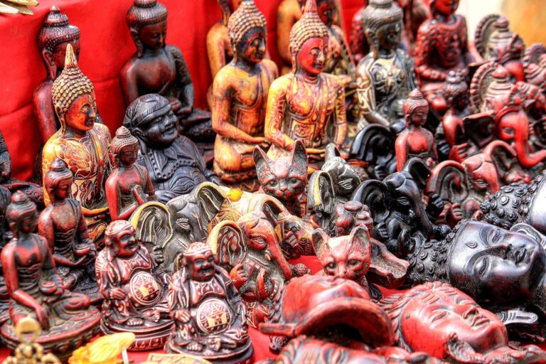 A collection of intricately carved wooden figurines, including several depictions of the Buddha and various animals, displayed against a red background.