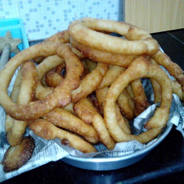 A pile of freshly fried golden-brown churros on a plate with paper towels, placed on a kitchen counter.