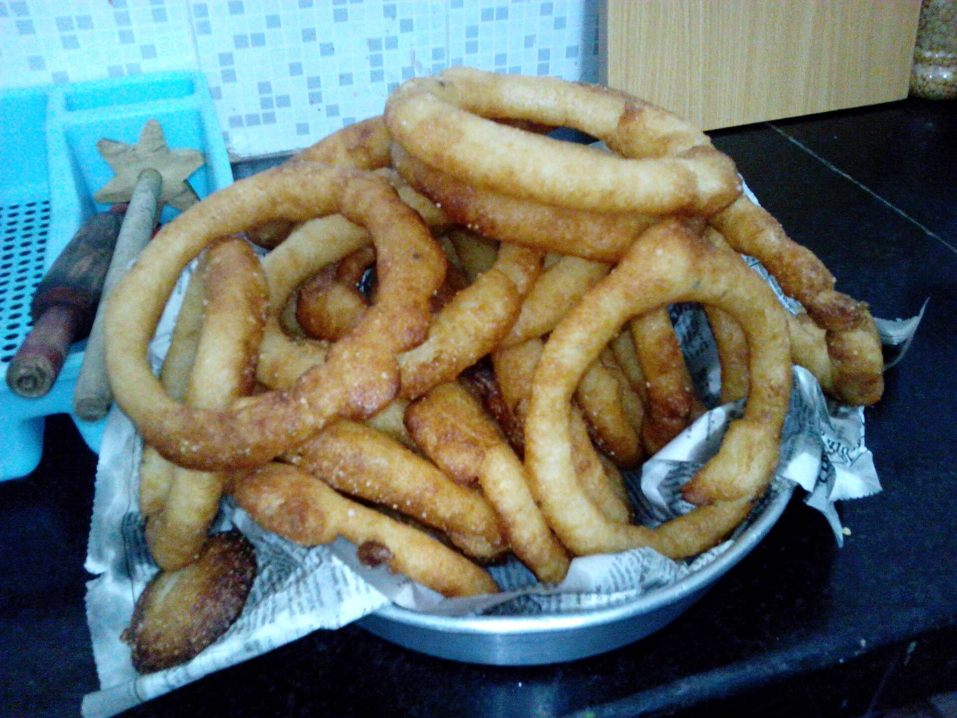 A pile of freshly fried golden-brown churros on a plate with paper towels, placed on a kitchen counter.