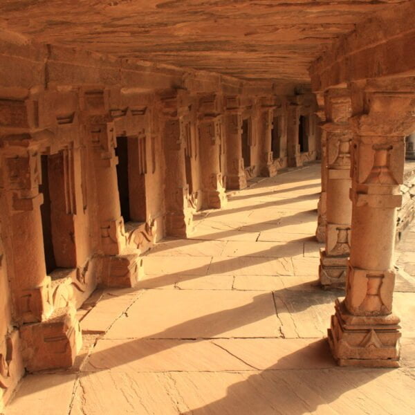 Stone colonnade with ornate pillars in warm sunlight, part of an ancient heritage structure, leading into the distance.