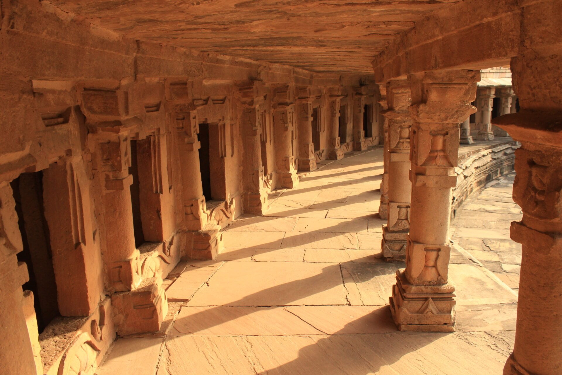 Stone colonnade with ornate pillars in warm sunlight, part of an ancient heritage structure, leading into the distance.
