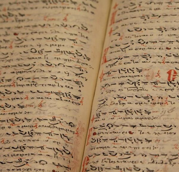 An open ancient manuscript with closely-written Arabic script in black ink, featuring occasional red markings for notation.