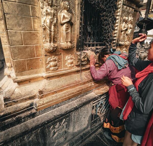 A woman holding a child observes and touches a golden relief on an ornate temple wall.