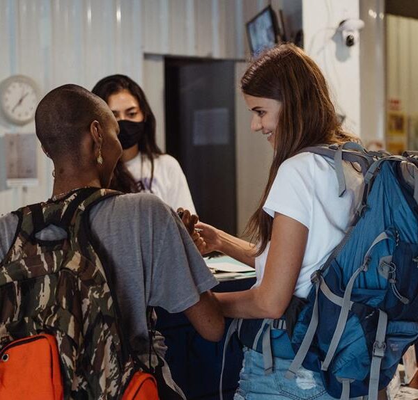 Two people with backpacks are engaging with a receptionist at a hostel check-in counter.