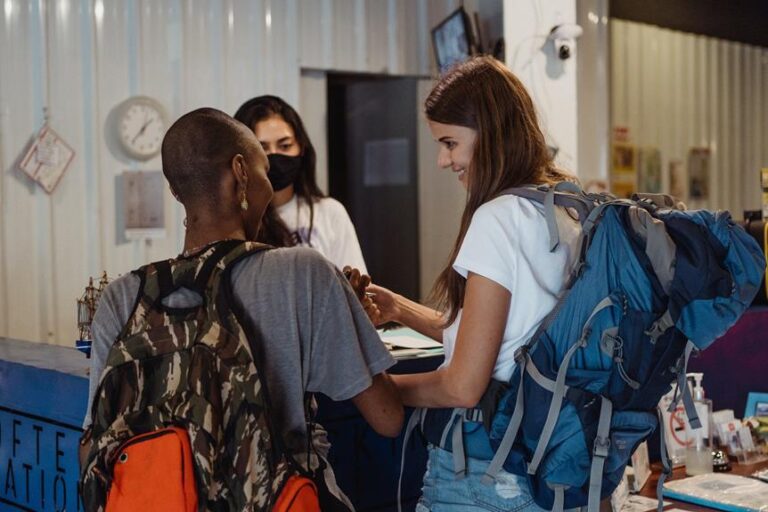Two people with backpacks are engaging with a receptionist at a hostel check-in counter.