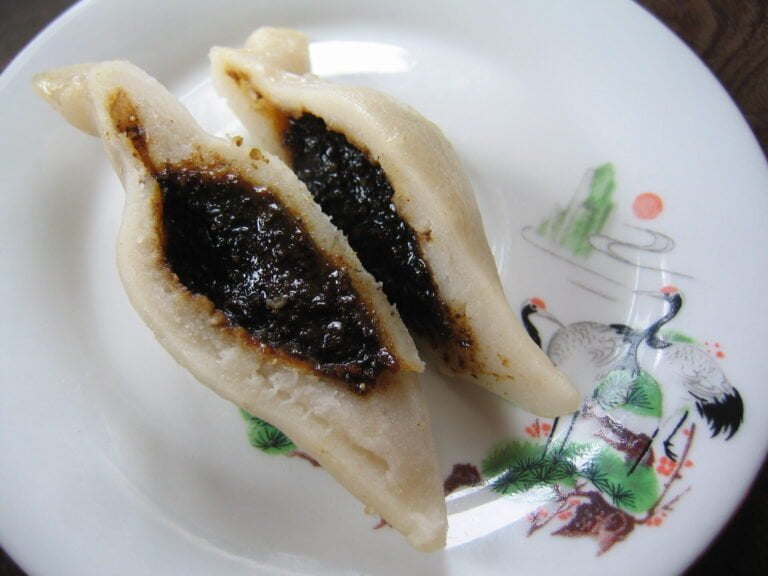 Two pieces of a cut open dumpling with black filling on a decorated white plate.