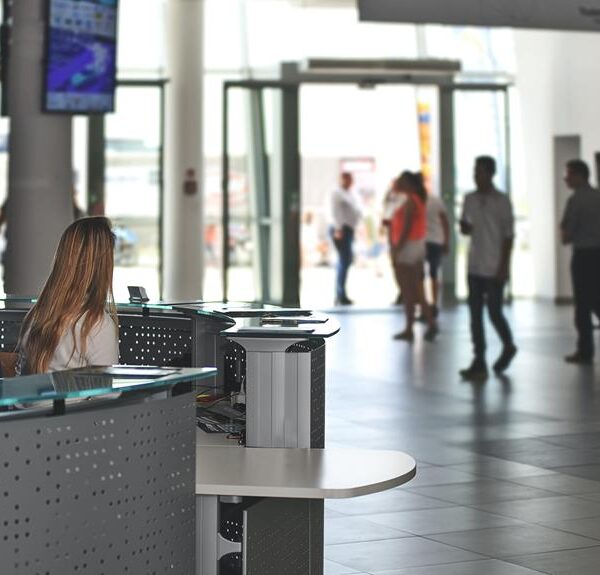 Reception area of a modern building with a female receptionist working at a desk and people walking in the background.