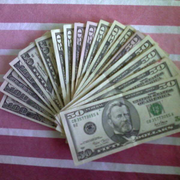 A fan of U.S. fifty and hundred dollar bills spread out on a pink and white striped fabric surface.