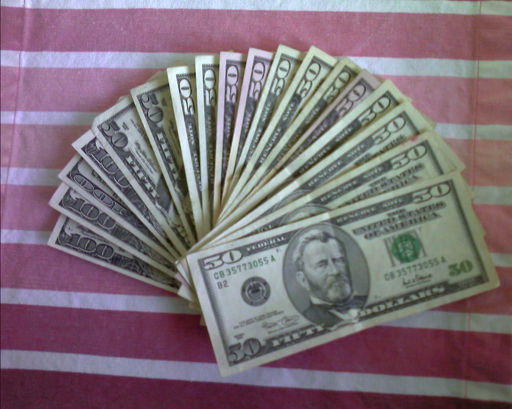 A fan of U.S. fifty and hundred dollar bills spread out on a pink and white striped fabric surface.