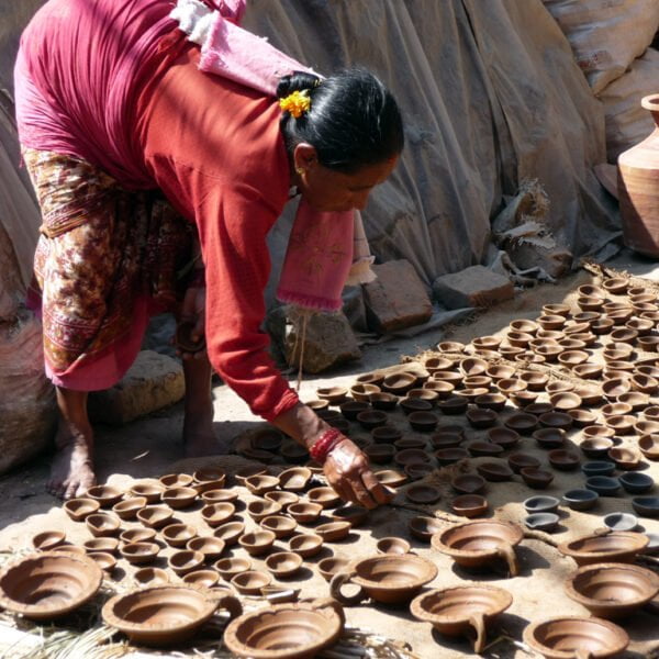A woman in traditional attire arranging freshly made earthen lamps on the ground to dry in the sun.