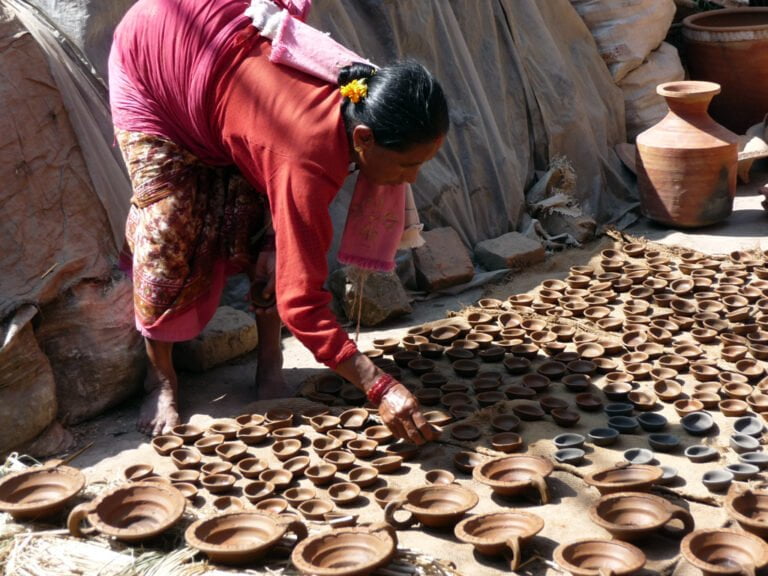 A woman in traditional attire arranging freshly made earthen lamps on the ground to dry in the sun.