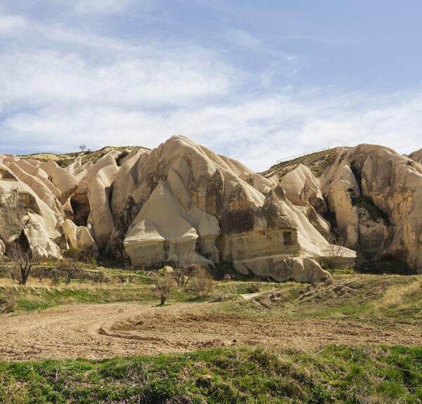 Eroded rock formations with various hues and patterns under a blue sky with scattered clouds in a grassy landscape.