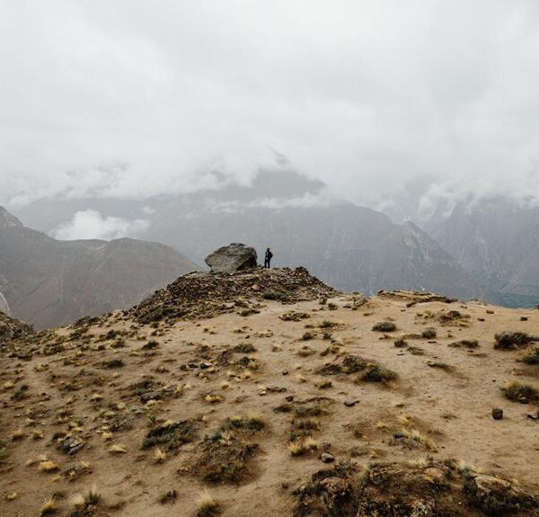 A person standing on a rocky outcrop overlooking a vast, misty mountainous landscape.