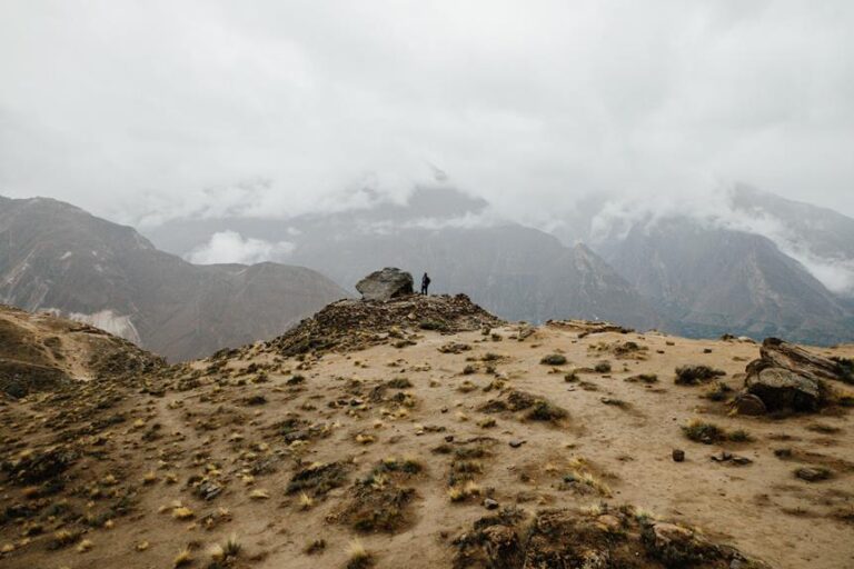 A person standing on a rocky outcrop overlooking a vast, misty mountainous landscape.