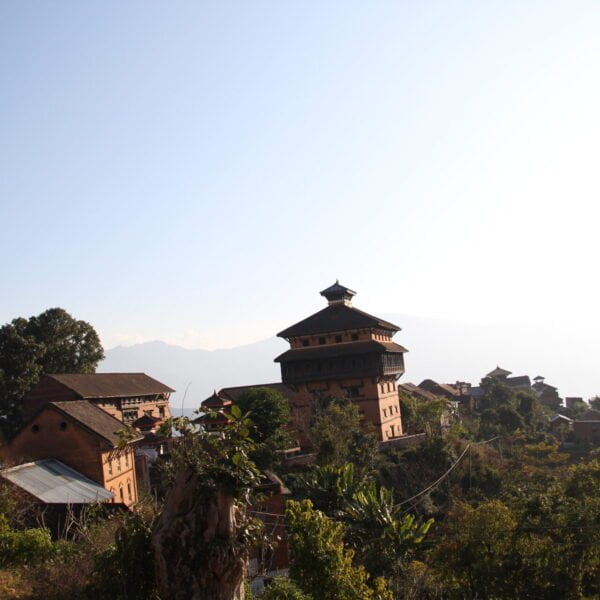 An ancient hilltop village with traditional multi-story buildings overlooking a mountain range under a clear sky.