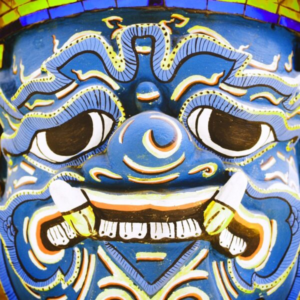 Close-up of a vibrant blue traditional demon mask with intricate patterns and fierce expression.