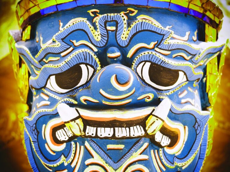 Close-up of a vibrant blue traditional demon mask with intricate patterns and fierce expression.