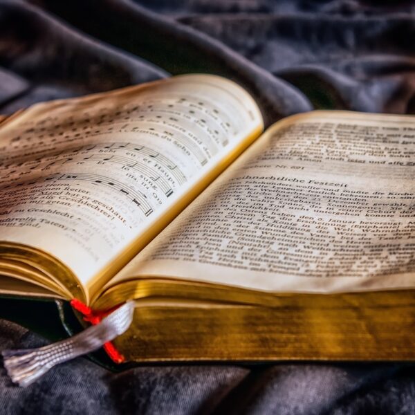 An open old book with gold-edged pages showing text and musical notation, resting on a dark, textured fabric.