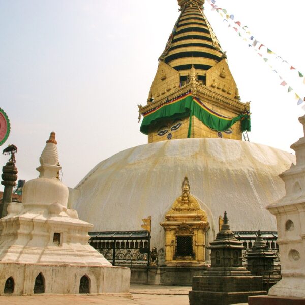 The image shows the Swayambhunath Stupa, also known as the Monkey Temple, in Kathmandu, Nepal, with a large white dome, a golden spire, colorful prayer flags, and smaller surrounding stupas and sculptures.