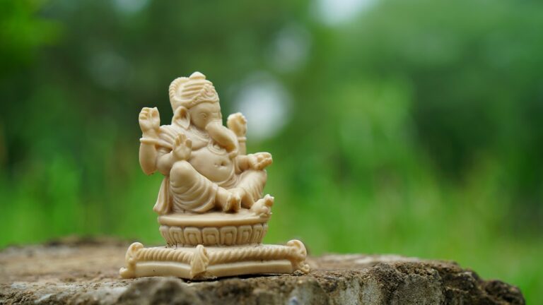 A small ivory-colored figurine of Lord Ganesha placed on a stone surface with a blurred green background.