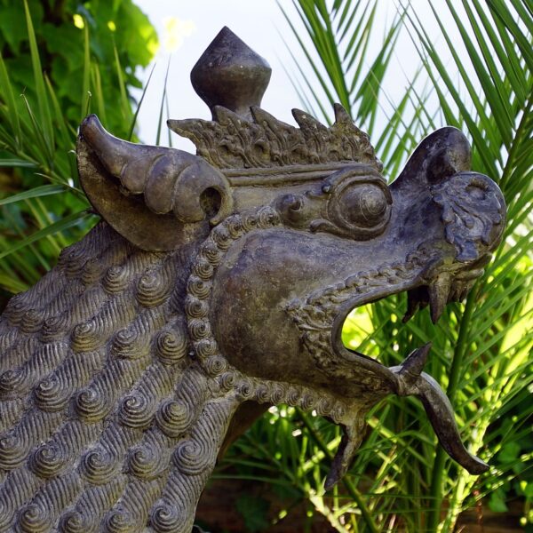 A close-up of a weathered metal dragon sculpture with intricate scale details, set against a background of green tropical foliage.