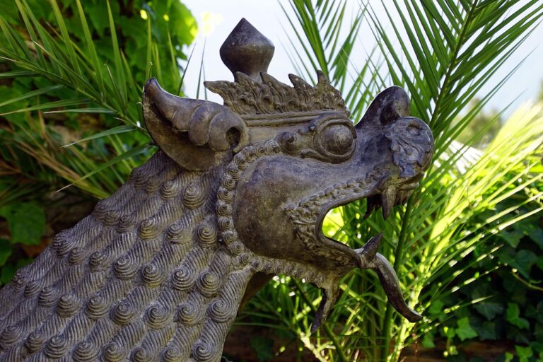 A close-up of a weathered metal dragon sculpture with intricate scale details, set against a background of green tropical foliage.