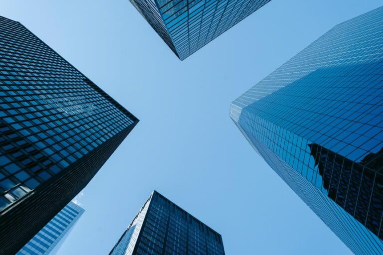 Low-angle view of several skyscrapers converging towards a clear blue sky.