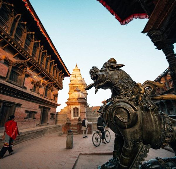 Bronze statue of a mythological creature in the foreground with ancient multi-tiered temple architecture and people in the background, taken during sunset.