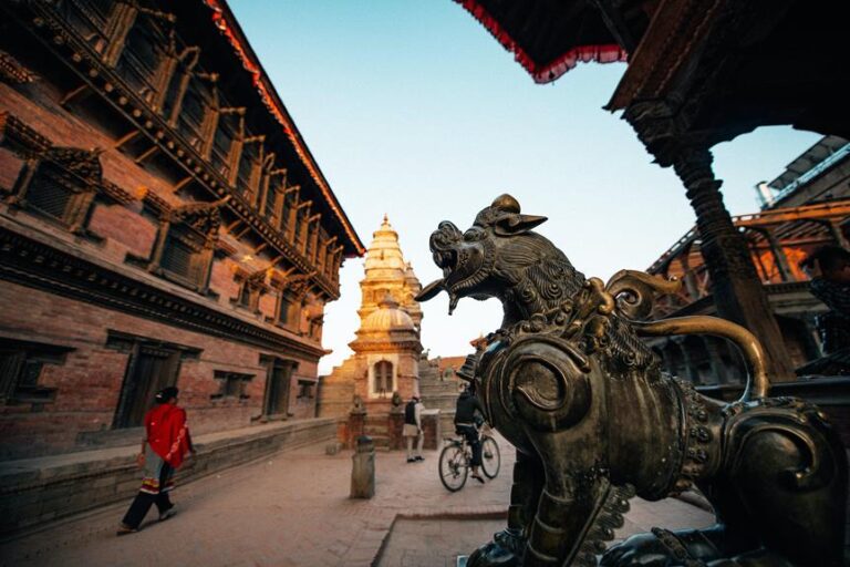 Bronze statue of a mythological creature in the foreground with ancient multi-tiered temple architecture and people in the background, taken during sunset.