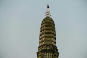 Top portion of a detailed stupa against a clear sky, featuring ornate decorative elements and a spire.