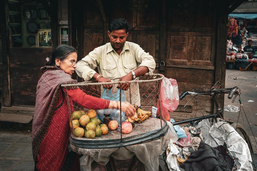 A street vendor with a cart full of fruits, including mangoes and bananas, is interacting with an older woman in a traditional saree, in an outdoor market setting with background shops and items on the street.