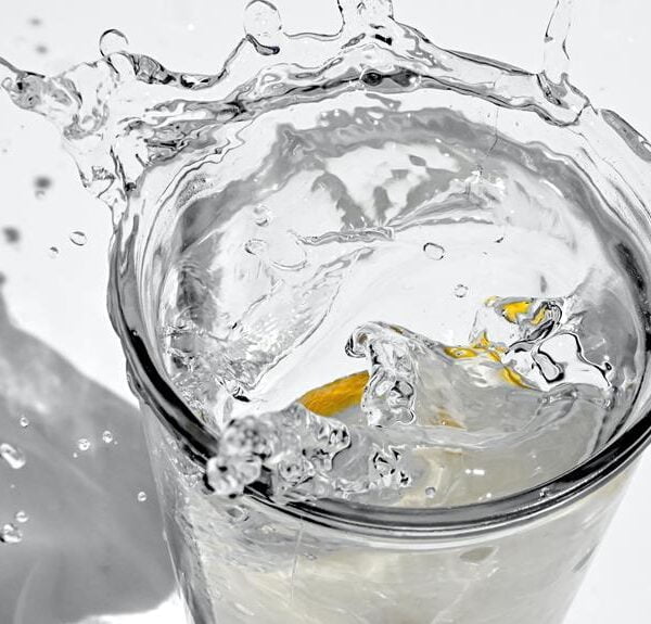 A lemon slice dropped into a glass of water, causing a dynamic splash with water droplets suspended in the air.