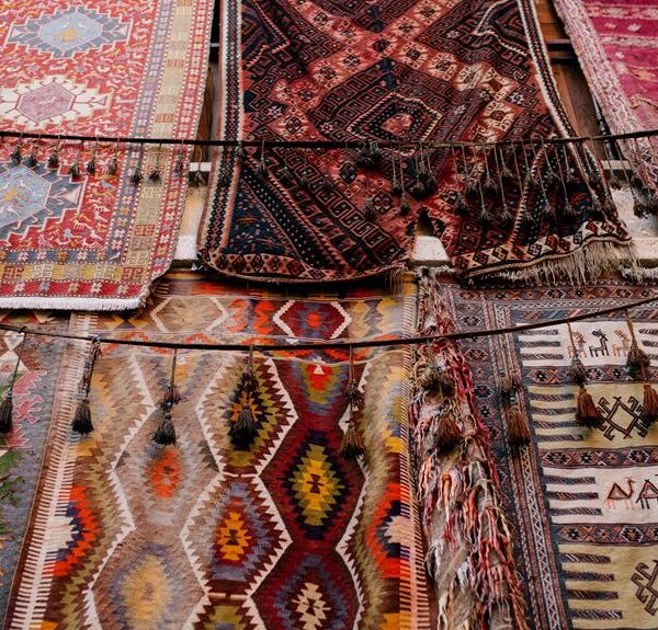 Various colorful handmade rugs with intricate patterns and designs hanging on display.