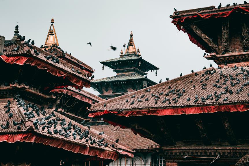 Ornate Nepalese temples with tiered roofs and golden spires, adorned with red fabric, and pigeons perched on the tiled surfaces.