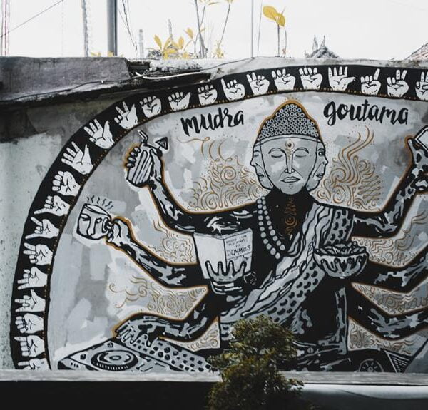 A monochrome mural featuring a stylized representation of a multi-armed figure with text labels "Mudra" and "Goutama". The artwork is adorned with patterns and symbolic imagery, displayed on an urban wall.